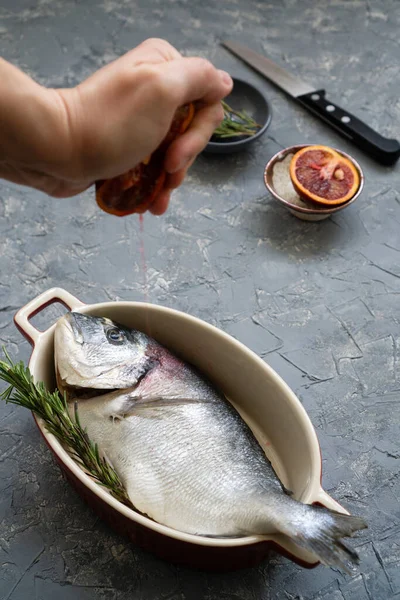 Cooking seafood with citrus and rosemary. The process of preparing fresh fish for roasting or frying with red oranges