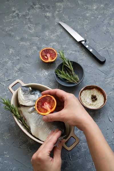 Fresh Moravian fish is gutted on a kitchen board with three red oranges. Cooking seafood with citrus and rosemary.
