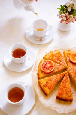 Üç kişilik tatlı kekli çay partisi. Eski bardaklar, çay tabakları ve bahar pembesi çiçekleriyle süslenmiş.