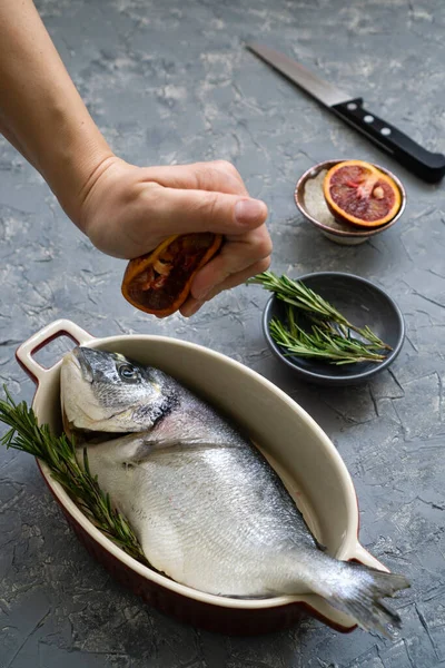 Cooking seafood with citrus and rosemary. The process of preparing fresh fish for roasting or frying with red oranges