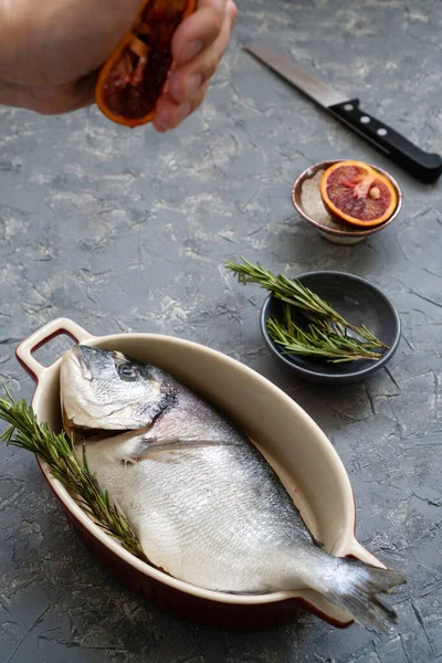 Cooking seafood with citrus and rosemary. The process of preparing fresh fish for roasting or frying with red oranges