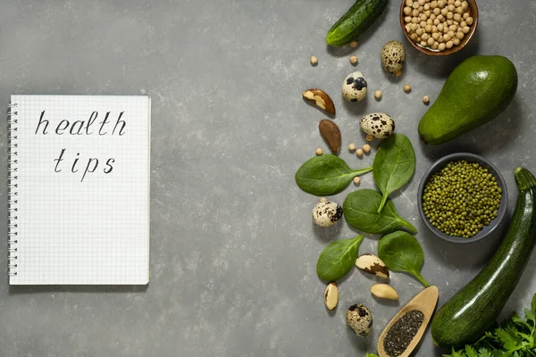 Diet plan with greens and fresh vegetables in a paper notebook on a gray table surface.