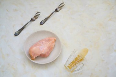 Çatal ve çiğ tavuk fileto tabağı. Kahvaltı, akşam yemeği ve şeffaf bir bardaktan masaya dökülen çay.