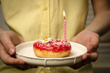 Üzerinde papatya desenli pembe bir bluz ve genç bir kızın ellerinde yanan bir mum olan bir pasta.