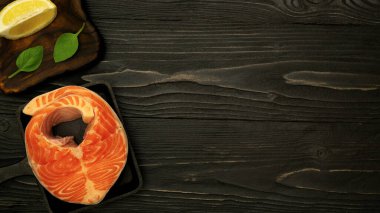 Mutfak masasının ahşap yüzeyinde limonlu, fesleğenli ve yağlı somon bifteği taze otlarla deniz ürünleri pişiriyorum.