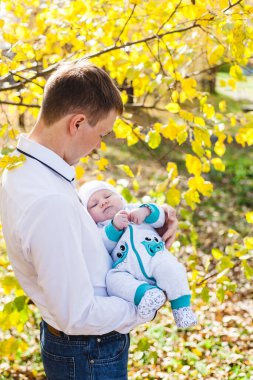 Bebekli bir baba, küçük bir çocuk sonbaharda parkta ya da ormanda yürüyor. Sarı yapraklar, doğanın güzelliği. Çocuk ve ebeveyn arasındaki iletişim.