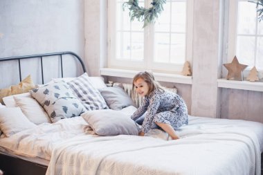 Oda yeni yıl için dekore edildi, küçük kız kardeşler yatakta oturuyor, oyun oynuyorlar, yastıklar, gülüyorlar, Noel 'i bekliyorlar.