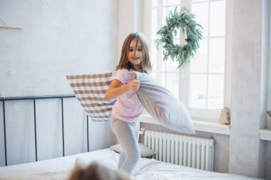 Oda yeni yıl için dekore edildi, küçük kız kardeşler yatakta oturuyor, oyun oynuyorlar, yastıklar, gülüyorlar, Noel 'i bekliyorlar.