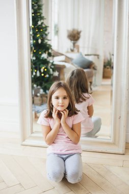 Oda yeni yıl için dekore edildi, bir Noel ağacı, aynanın yanında oturan bir kız, hediyeleri bekliyor.