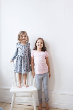 Kız kardeşler beyaz bir duvar ve sandalyeye yakın, boy ölçümü, oyunlar, kim daha uzun, kahkaha, tartışmalar, duygular