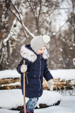 Kız çocuğu mavi ceketli, gri şapkalı, kar taneli, soğuk hava, bebek gülüşlü, kış ormanlarında yürüyor.