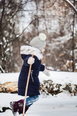 Kız çocuğu mavi ceketli, gri şapkalı, kar taneli, soğuk hava, bebek gülüşlü, kış ormanlarında yürüyor.