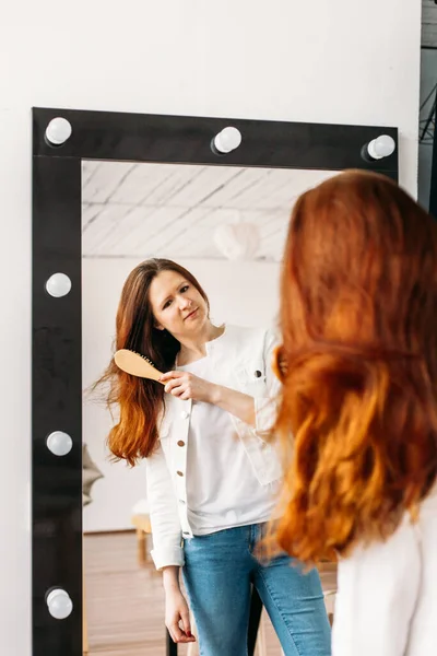 鏡の前にはヨーロッパ人の女の子が立っていて櫛や髪の毛の美しさケア — ストック写真