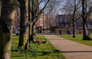 Londra, Birleşik Krallık - 24 Şubat 2019: İnsanlar parktaki yeşil bir çimenlikte oturup rahatlıyorlar. Parkta yaz öğleden sonra. Tam olarak odaklanamıyorum..