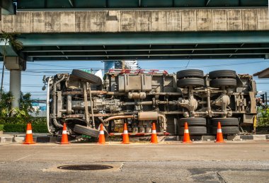Bir kavşağın üzerindeki köprünün altındaki yolda devrilmiş bir konteynır taşıyan kamyonun görüntüsü..