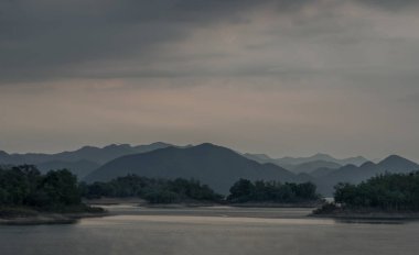 Gün doğumunda veya günbatımında arkaplanda dağlar olan göl kıyısı manzarası. Seçici odak.