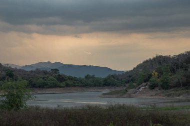 Gün doğumunda veya günbatımında arkaplanda dağlar olan göl kıyısı manzarası. Seçici odak.