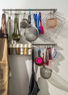 Mutfak aletleri, mutfak aletleri asılı metal parmaklıklar, önlük ve baharat mutfakta beyaz bir duvarın önünde. Mutfağın içini kapatıyoruz. Seçici odak.