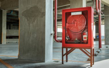 Otoparkta kırmızı bir itfaiye malzemesi dolabı veya yangın söndürme dolabı bulunuyor. Acil durum yangın söndürücü, rulo boru, yangın musluğu ve su hortumları, önce güvenlik kavramı. Seçici odak.