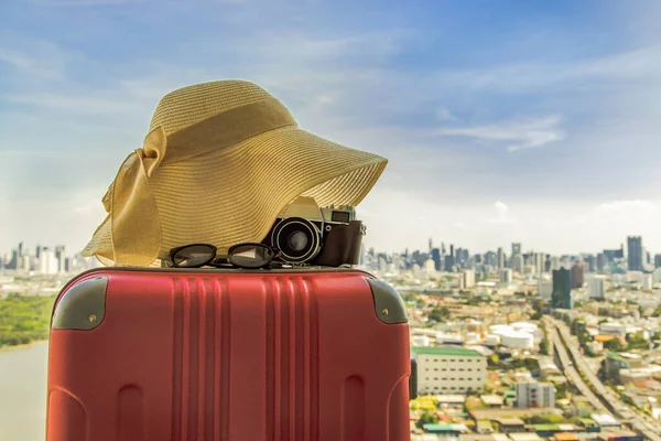 Vacation and travel. Suitcase or luggage bag with hat, Photo camera and Sun glasses with city view background. Summer vacation holidays traveling design concept. Free Space, Selective focus.