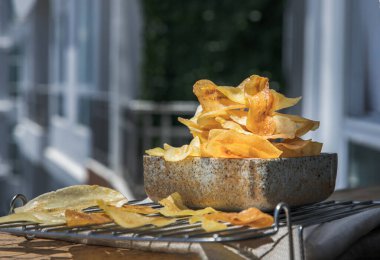 Birçok ev yapımı muz cipsi, balkondaki ahşap masadaki seramik kasede yeni bitti. Muzlu tatlı, uzun muz cipsi, metin için boş yer, seçici odaklanma..