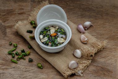 Tayland acılı balık sosu ve Tayland yeşili ve kırmızı biberli malzemeler, eski ahşap masada seramik beyaz bardakta sarımsak. Uzayı kopyala, odağı seç.