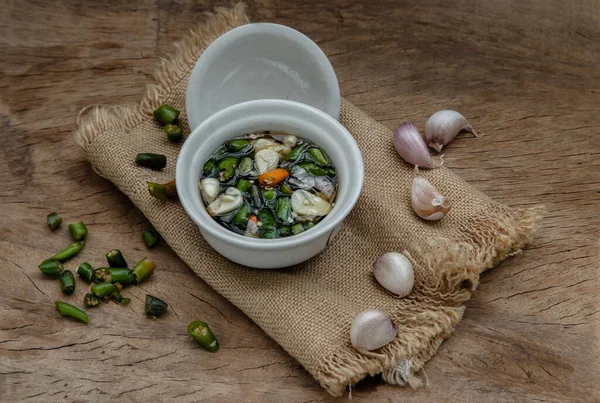 Tayland acılı balık sosu ve Tayland yeşili ve kırmızı biberli malzemeler, eski ahşap masada seramik beyaz bardakta sarımsak. Uzayı kopyala, odağı seç.