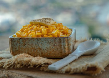 Bir tutam tereyağlı ve baharatlı kızarmış mısır seramik kâse ve kaşıkta karabiber serpiştirilmiş. Sağlıklı gıda konsepti, seçici odaklanma.