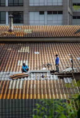 Bangkok, Tayland - 28 Mayıs 2021: Hasarlı fabrika çatısında fayans tamir eden iki işçi. Seçici odak.