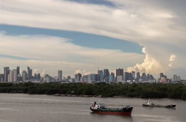 Bangkok, Tayland - 26 Haziran 2021: Arka planda yeşil orman ve gökdelenlerle Chao Phraya Nehri 'nin ortasına park edilmiş iki kargo gemisi. Tam olarak odaklanamıyorum..