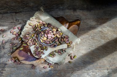 Kabuklu şam fıstığı yığını eski ahşap arka plandaki çuval bezinin üzerindeki çekirdekler. Pistacia 'nın kurumuş tohumları ve olgun meyveleri, Üst Görüş, Kopyalama alanı, Seçici odak.