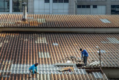 Bangkok, Tayland - 28 Mayıs 2021: Hasarlı fabrika çatısında fayans tamir eden iki işçi. Seçici odak.