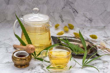 Rahatlatıcı ve keyifli bir fincan kenevir bitkisel çay ve yeşil marihuana yapraklı kök mermer masa üzerinde bal ile uyku ve endişe için tıbbi amaçlar. Bitki çayı ve sağlıklı içecek konsepti. Seçici odak.