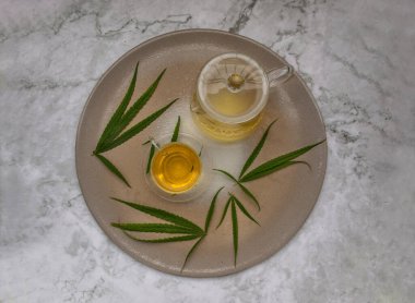 Uyku ve anksiyete için mermer masada yeşil marihuana yapraklı bir fincan kenevir çayı ve kök ile ferahlatıcı ve tadını çıkarın. Bitki çayı ve sağlıklı içecek konsepti. Üst Görünüm, Seçici Odaklanma.