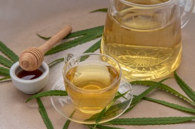 Rahatlatıcı ve keyifli bir fincan kenevir bitkisel çay ve yeşil marihuana yapraklı kök mermer masa üzerinde bal ile uyku ve endişe için tıbbi amaçlar. Bitki çayı ve sağlıklı içecek konsepti. Boşluğu kopyala, Seçici odak.