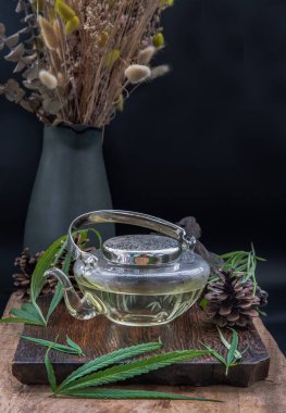 Çaydanlıkta esrarlı bitki çayı ve ahşap arka planda yeşil marihuana yaprakları. Uyku ve endişe için tıbbi amaçlar. Bitki çayı ve sağlıklı içecek konsepti. Boşluğu kopyala, Seçici Odaklanma.