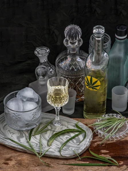 Buzlu, soğuk marihuana kenevir CBD, kristal berrak bir bardakta, ahşap zemin üzerinde yeşil marihuana yaprağı olan bir içecek. Kenevir kokteyli, uyku ve anksiyete için tıbbi amaçlar, bitkisel ve sağlıklı içecek konsepti. Seçici Odaklanma.