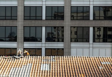 Bangkok, Tayland - 21 Mayıs 2021: Hasarlı fabrika çatısında fayans tamir eden iki işçi. Seçici odak.