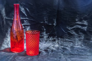 Renkli kırmızı cam bardak ve su içmek için kırmızı cam şişe ve siyah arka planda yüzey yansımaları. Boşluğu kopyala, Seçici odak.