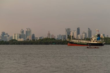 Bangkok, Tayland - 26 Mar 2020: Nehrin ortasına ve Chao Phraya Nehri kıyısındaki yeşil bir ağacın önüne park edilmiş iki kargo gemisi.