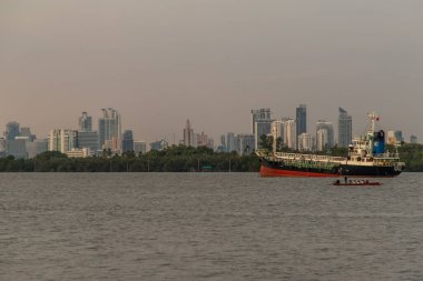 Bangkok, Tayland - 26 Mar 2020: Nehrin ortasına ve Chao Phraya Nehri kıyısındaki yeşil bir ağacın önüne park edilmiş iki kargo gemisi.
