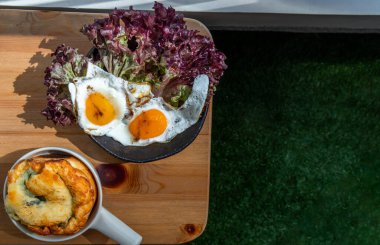 Ispanaklı brioche ile kahvaltı, iki sahanda yumurta, balkondaki ahşap masada meşe yaprağı marulu. Seçici odak.