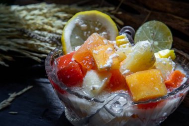 Süt ve yulaf ezmeli tropikal taze meyve salatası koyu arka planda cam bir kasede. Sağlıklı bir kahvaltı, sağlıklı bir vejetaryen yemeği. Seçici odak.