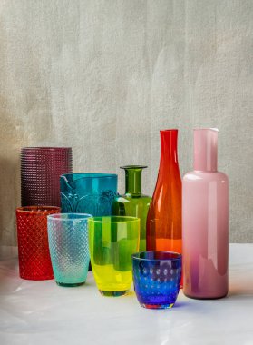 Birçok farklı cam kavanoz, cam bardak ve pembe masa örtüsüne yansıyan yüzey yansımaları. Farklı cam eşyalar grubu, seçici odak.