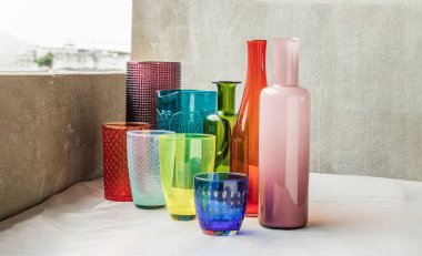 Birçok farklı cam kavanoz, cam bardak ve pembe masa örtüsüne yansıyan yüzey yansımaları. Farklı cam eşyalar grubu, seçici odak.