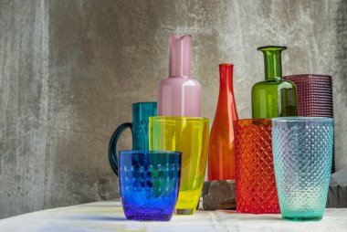 Birçok farklı cam kavanoz, cam bardak ve pembe masa örtüsüne yansıyan yüzey yansımaları. Farklı cam eşyalar grubu, seçici odak.