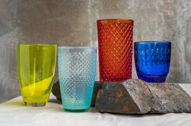 Birçok farklı cam bardak ve pembe masa örtüsüne yüzeysel yansımalar. Farklı cam eşyalar grubu, seçici odak.