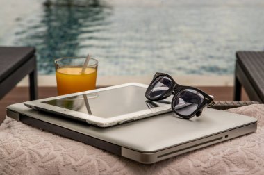 Havuz kenarında dinlenme anı. Laptop ve tablet üzerinde çalışmaya ara ver ve ferahlatıcı olarak taze portakal suyunun tadını çıkar. Açık yüzme havuzu geçmişi. boş zaman aktivitesi.