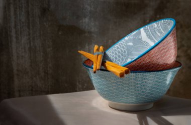 Pembe masa örtüsünün üzerinde tahta çubuklar olan iki seramik kasesi. Seramik tablo takımı, Güzel düzenleme, Kopyalama alanı, Seçici odak.