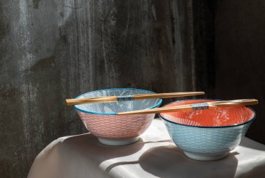 Pembe masa örtüsünün üzerinde tahta çubuklar olan iki seramik kasesi. Seramik tablo takımı, Güzel düzenleme, Kopyalama alanı, Seçici odak.